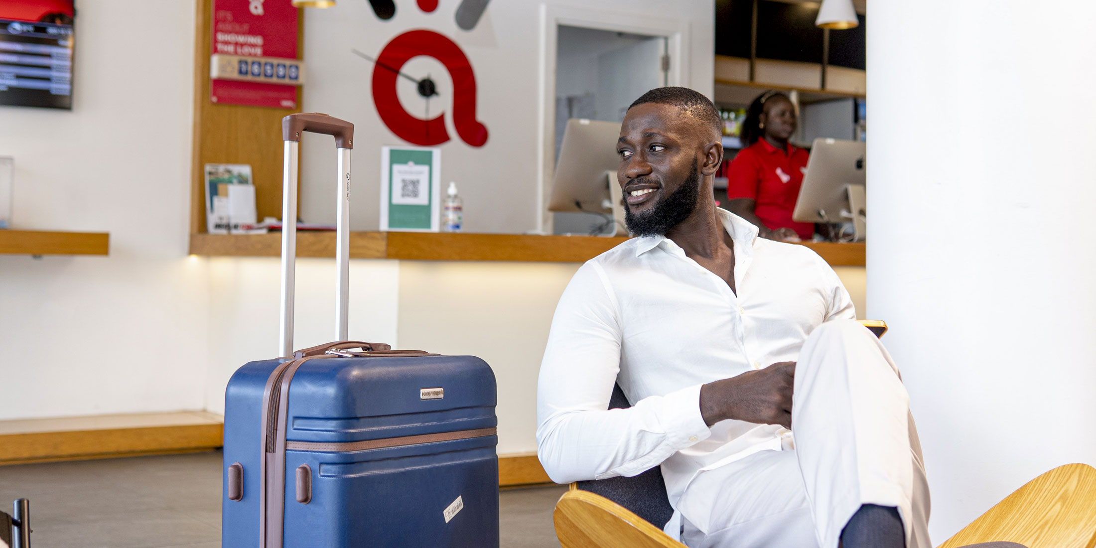 a man sits in a chair with a blue suitcase in front of a red a sign
