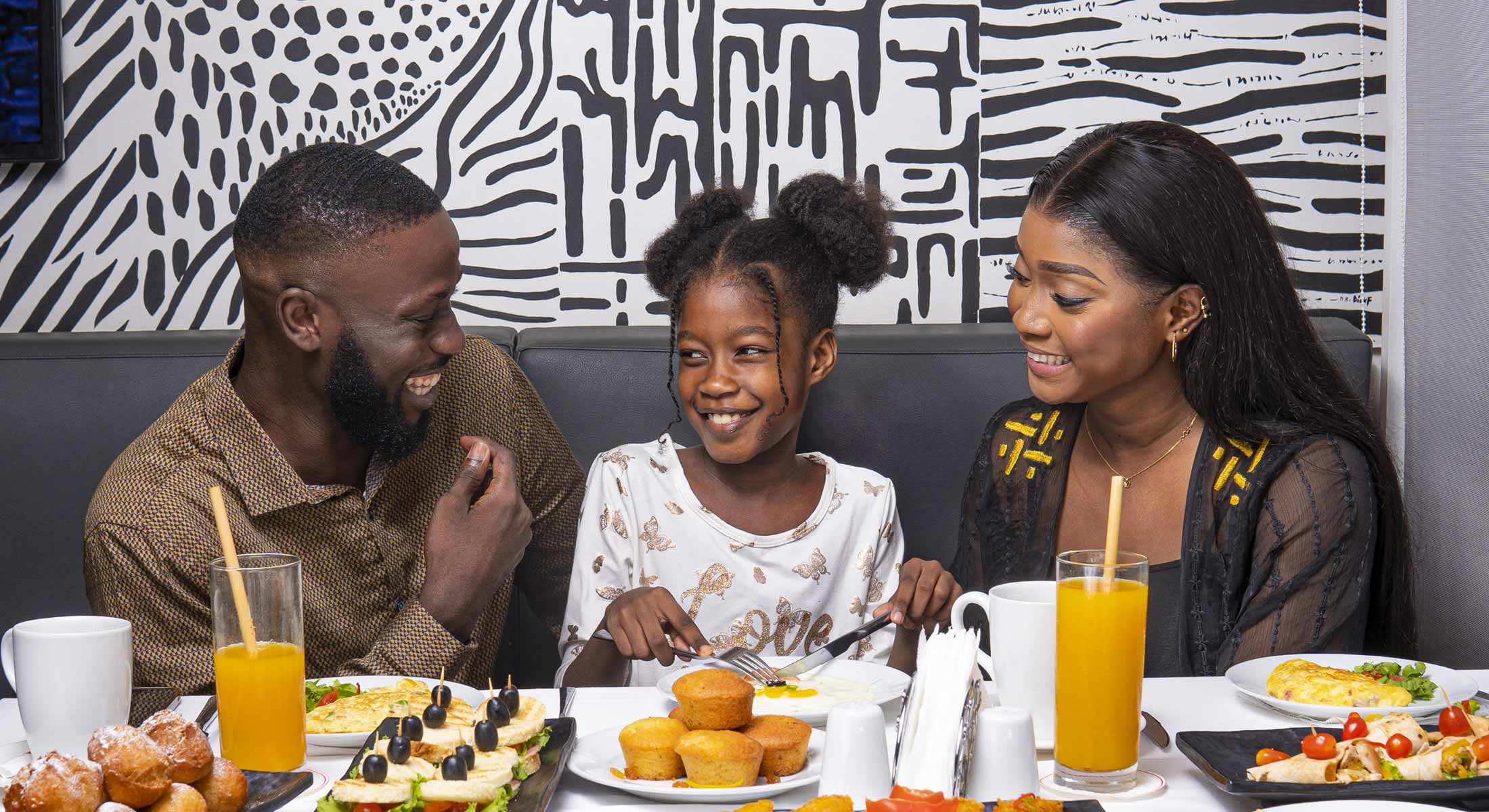 a family sits at a table eating food and drinking orange juice