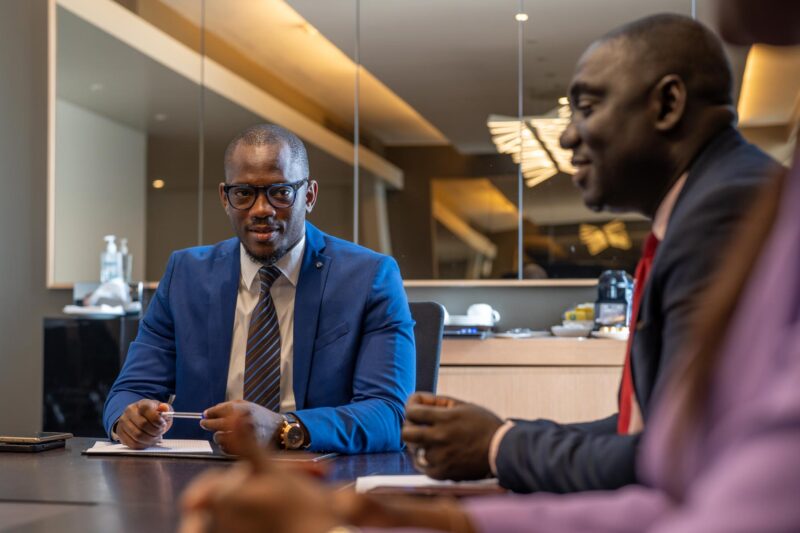 a man in a blue suit sits at a table with two other men