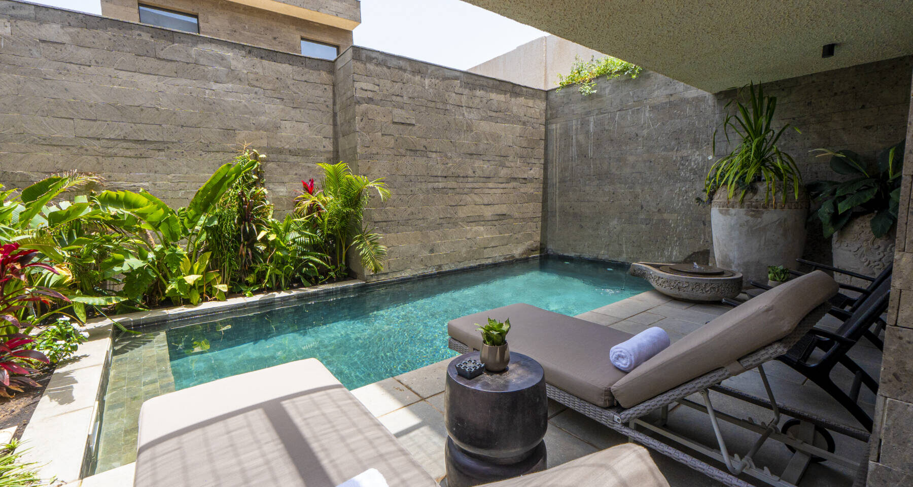 Espace piscine luxueux avec chaises longues et végétation luxuriante.