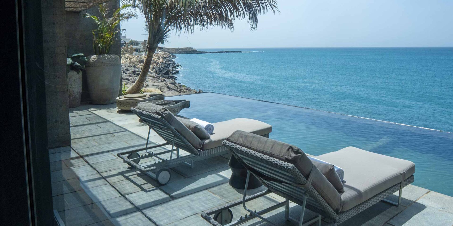 Vue sur l'océan avec des chaises longues au bord d'une piscine à débordement.