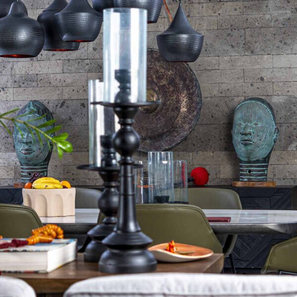 Salle à manger avec un mur en pierre, des suspensions sombres et une décoration d'inspiration africaine.
