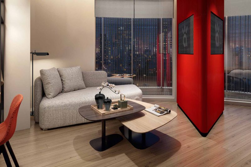 Modern living room with a gray sofa, coffee tables, and a vibrant red partition wall.