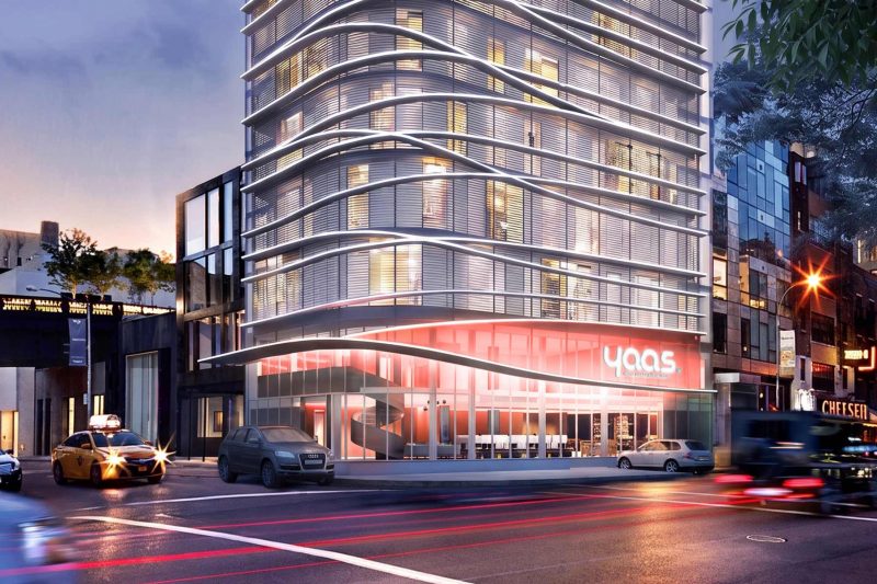 Hôtel moderne à la façade ondulée, situé à un carrefour urbain, vu de nuit.